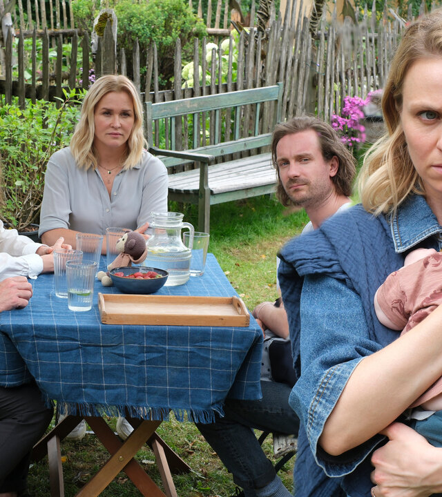 "Lena Lorenz - Vertauscht": Im Garten des Lorenzhofes sitzen Gregor (Nicholas Reinke) und Mareike Völler (Anja Antonowicz),  Lena Lorenz (Judith Hoersch) und Raffael Vollmer (Max Rothbart). Alle schauen Annika (Teresa Rizos) hinterher, die ihr Baby an sich drückt und mit besorgtem Gesichtsausdruck den Tisch verlässt.