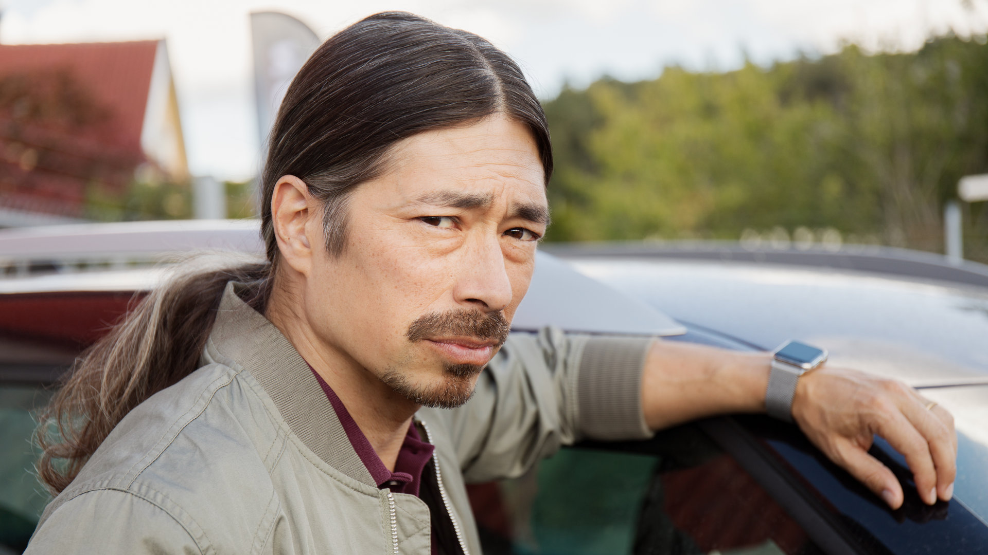 "Detective No. 24 - Suchen und Finden": Mats (Kristofer Kamiyasu) steht neben einem Auto. Sein linker Arm liegt auf dem Dach.