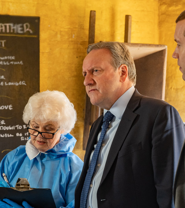 "Inspector Barnaby - Ein Körnchen Wahrheit": Fleur Perkins (Annette Badland), in blauem Schutzanzug, schreibt auf einem Klemmbrett in ihrer Hand, Inspector John Barnaby (Neil Dudgeon) und sein Assistent DS Jamie Winter (Nick Hendrix) stehen neben ihr. Im Hintergrund ist eine mit weißer Kreide beschriftet Tafel.