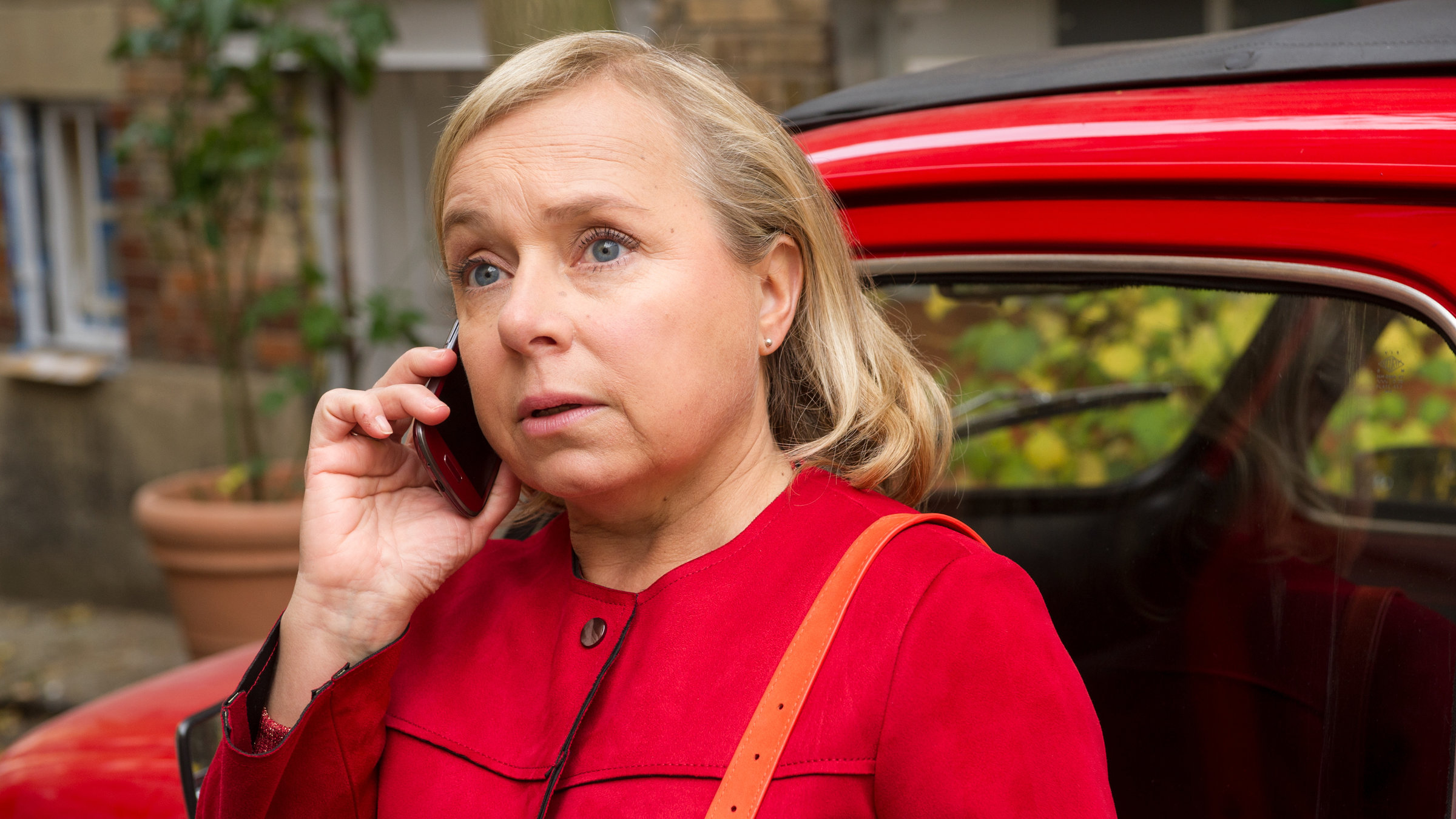 "Dr. Klein - Totalschaden": Valerie (ChrisTine Urspruch) steht neben der Fahrertür ihres roten Autos und telefoniert. Sie trägt eine rote Jacke.
