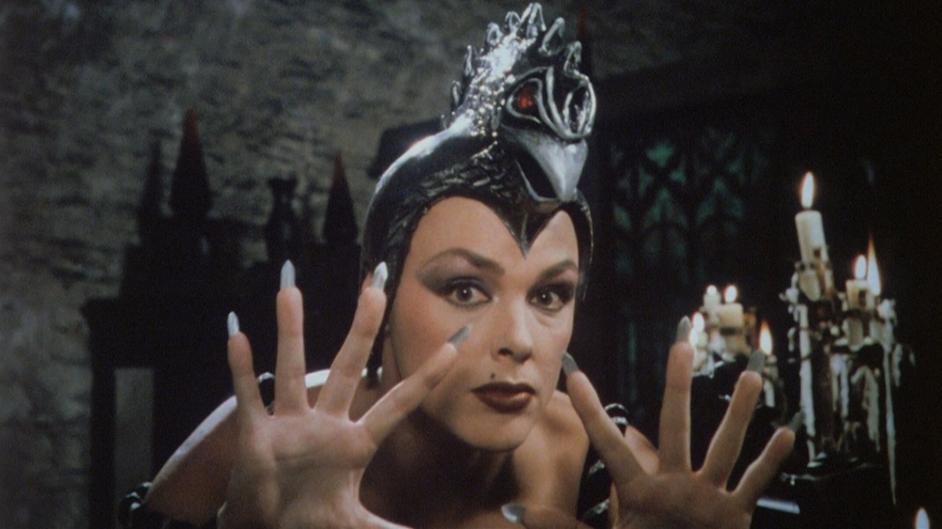 "Prinzessin Fantaghirò - Teil 3": Nahaufnahme der Schwarzen Königin (Brigitte Nielsen), die die gespreizten Finger in die Höhe streckt. Auf dem Kopf trägt sie einen Helm, der mit einem Vogelkopf mit roten Augen verziert ist.