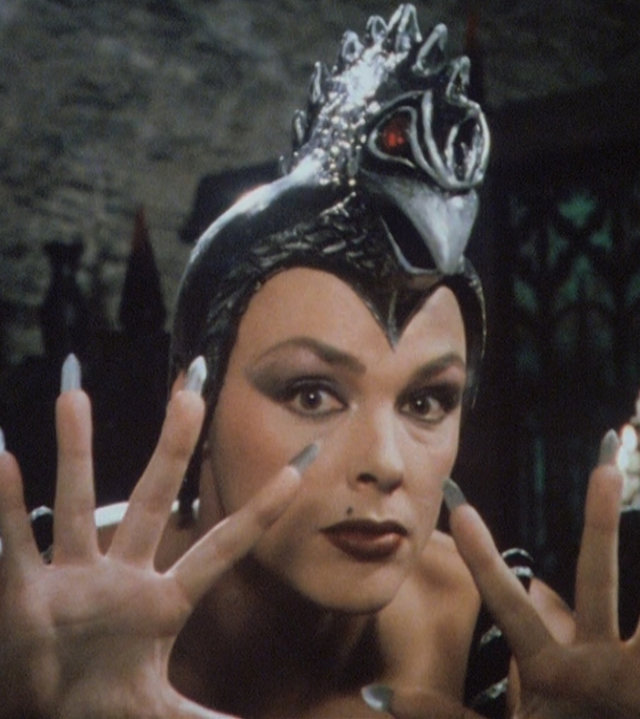 "Prinzessin Fantaghirò - Teil 3": Nahaufnahme der Schwarzen Königin (Brigitte Nielsen), die die gespreizten Finger in die Höhe streckt. Auf dem Kopf trägt sie einen Helm, der mit einem Vogelkopf mit roten Augen verziert ist.