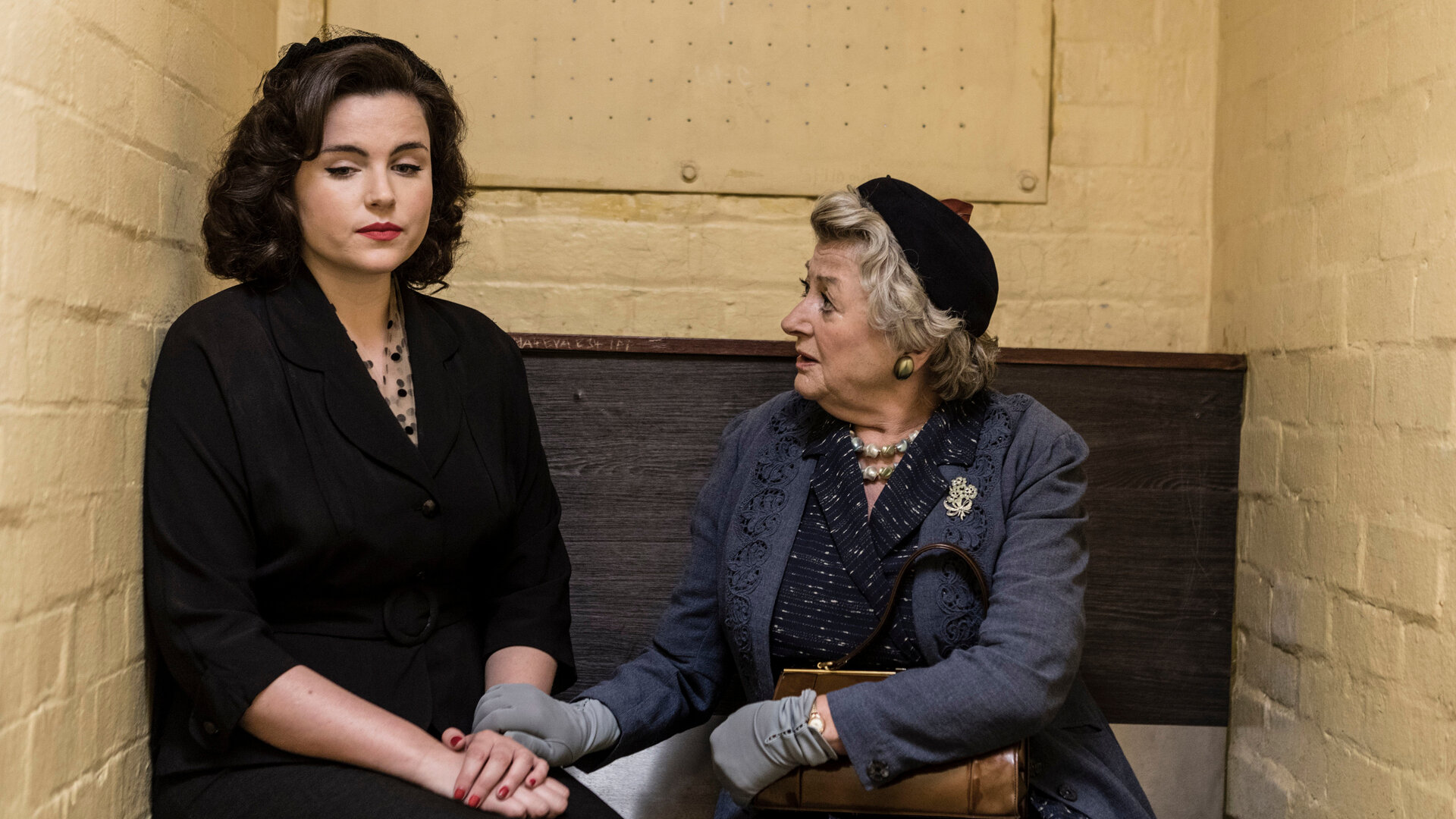 "Father Brown - Die Waage der Gerechtigkeit": Bunty (Emer Kenny) und Mrs McCarthy (Sorcha Cusack) sitzen nebeneinander in einer Gefängniszelle. Bunty hat einen traurigen Gesichtsausdruck.