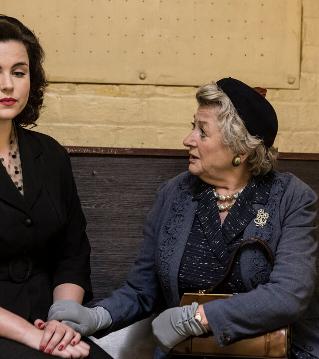 "Father Brown - Die Waage der Gerechtigkeit": Bunty (Emer Kenny) und Mrs McCarthy (Sorcha Cusack) sitzen nebeneinander in einer Gefängniszelle. Bunty hat einen traurigen Gesichtsausdruck.