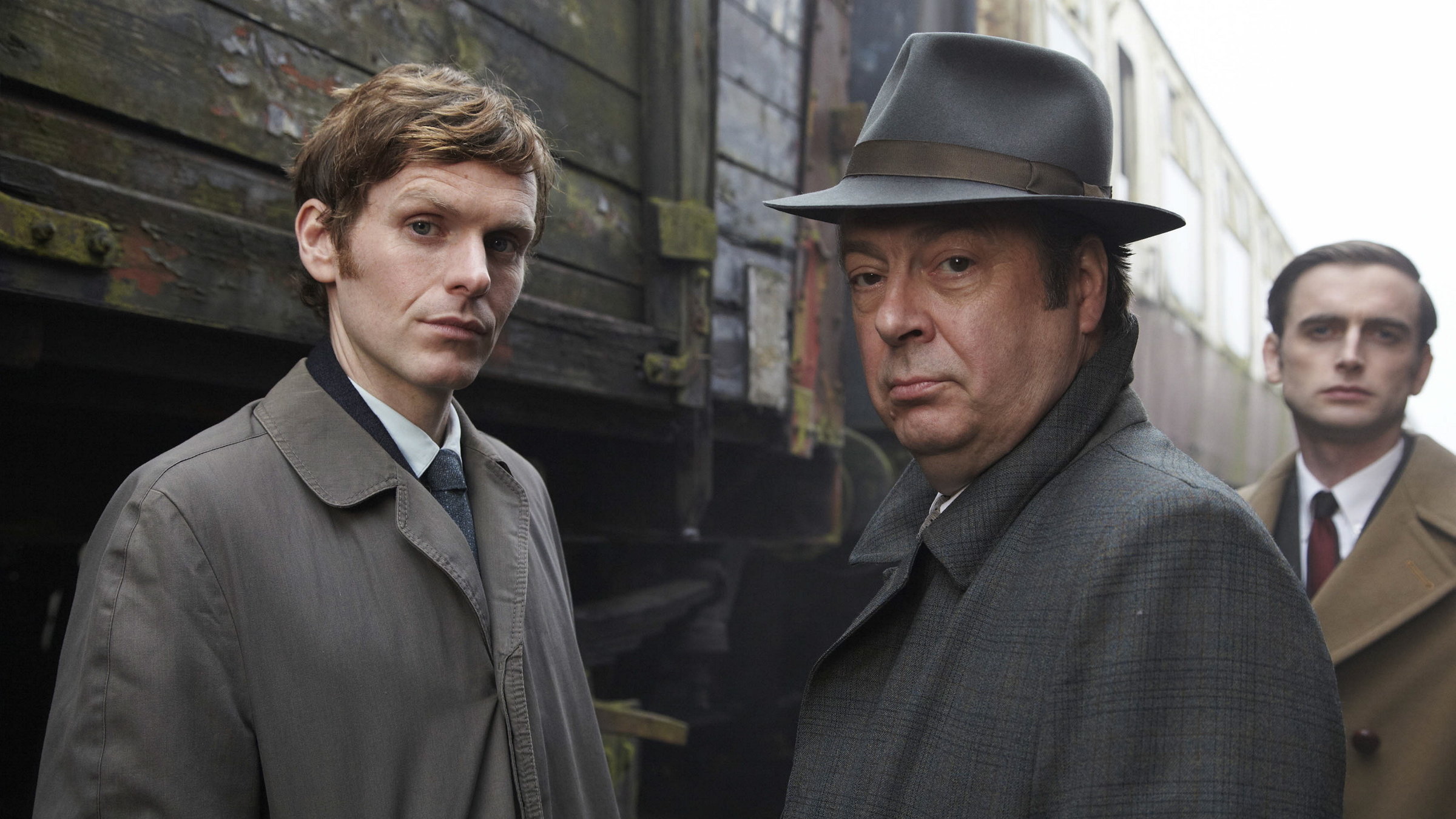 "Der junge Inspektor Morse - Mord nach Noten": Endeavour Morse (Shaun Evans), DI Fred Thursday (Roger Allam) und Peter Jakes (Jack Laskey) posieren vor stehenden Bahnwaggons