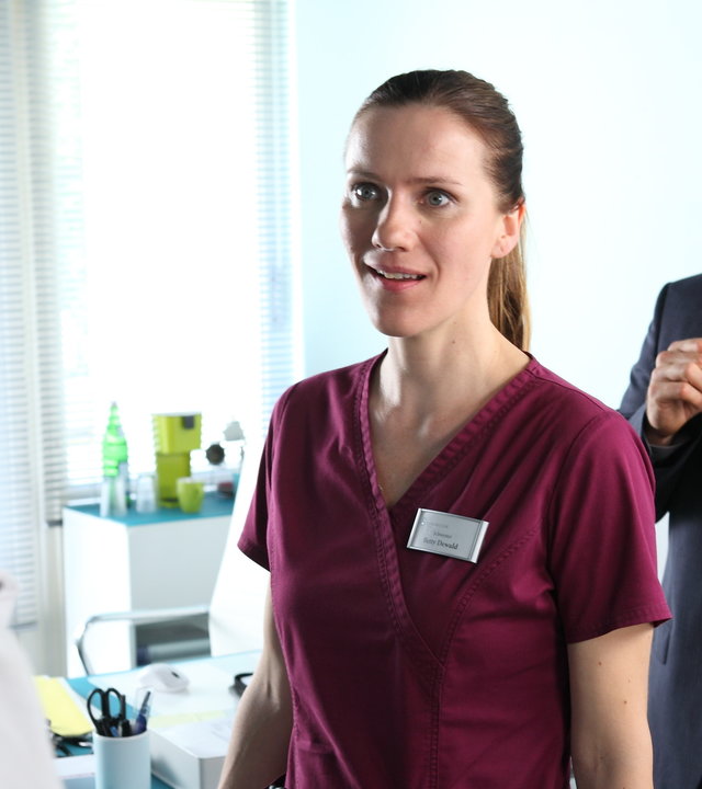 "Bettys Diagnose - Kein Tag wie jeder andere": Betty (Bettina Lamprecht) steht Dr. Behring (Maximilian Grill) in einem Zimmer gegenüber und schaut ihn ungläubig an. Hinter ihnen steht Jan Petersen (Matthias Ziesing), der gerade eine Tasse Kaffee trink und das Geschehen beobachtet.