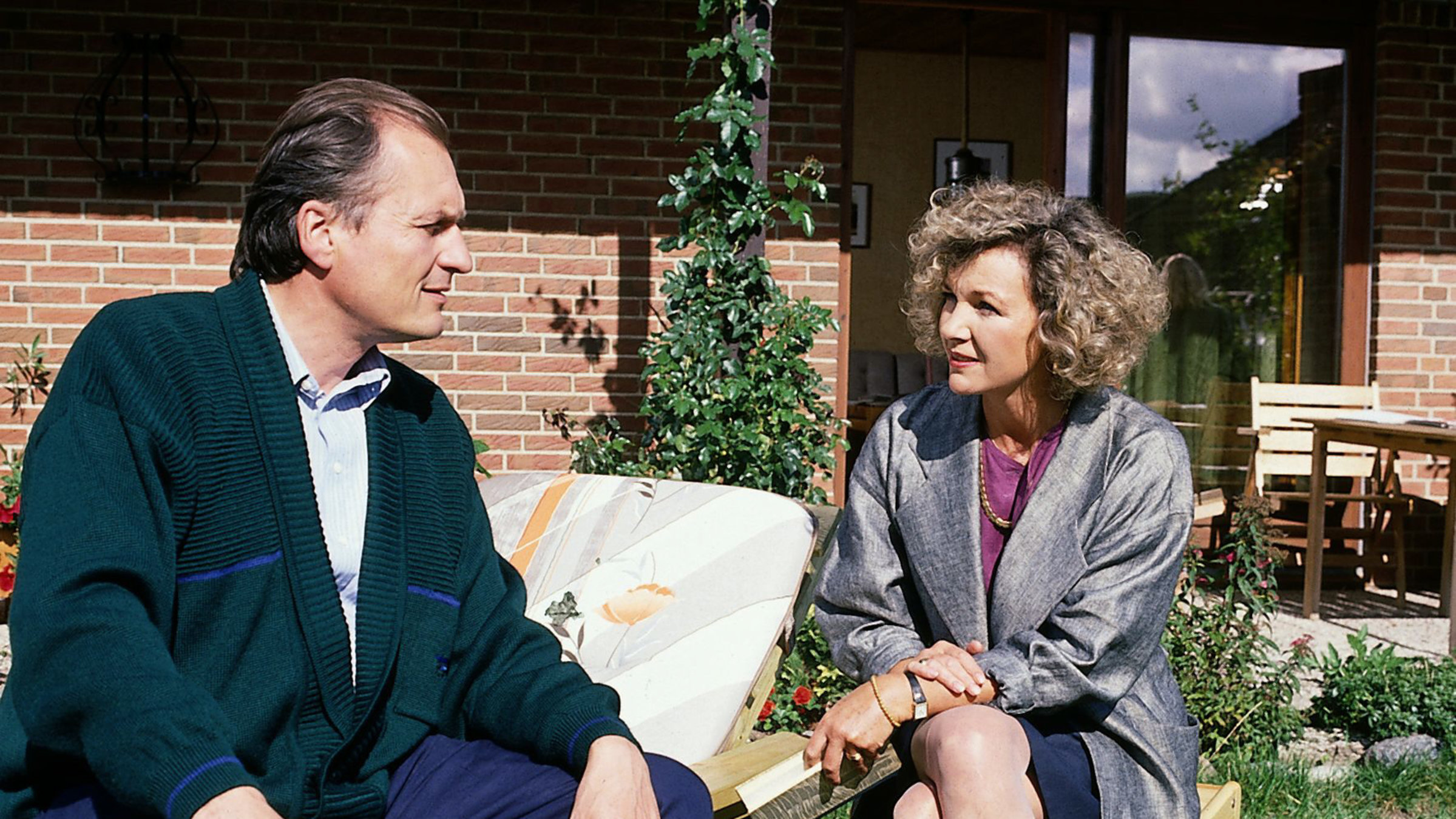 "Der Landarzt - Ein Fremder im Haus": Annemarie Mattiesen (Gila von Weitershausen) sitzt neben Dr. Schneider (Dietrich Mattausch) in einem Garten und schaut ihn besorgt an.