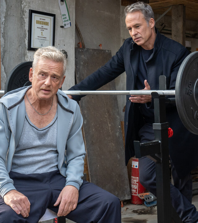 "SOKO Leipzig - Nadelstiche": Thilo Neuenburg (Thomas Huber) sitzt in einem Schuppen auf einer Hantelbank mit dem Rücken zu Jan Maybach (Marco Girnth). Die beiden Männer sprechen miteinander.