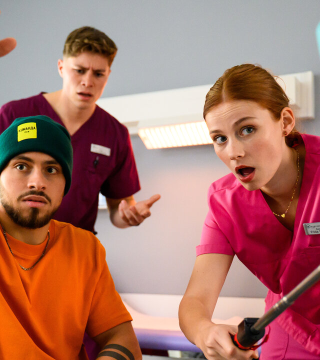 "Bettys Diagnose - Große Kinder, große Sorgen": In einem Raum in der Klinik: Amir (Angelo Alabiso) hält ein Jo-Jo in der Hand und wird dabei von Frida (Johanna Hens) mit dem Handy gefilmt. Sie hält dazu einen Selfiestick in seine Richtung. Ivo (Oscar Nadermann) steht im Hintergrund und beobachtet das Geschehen.