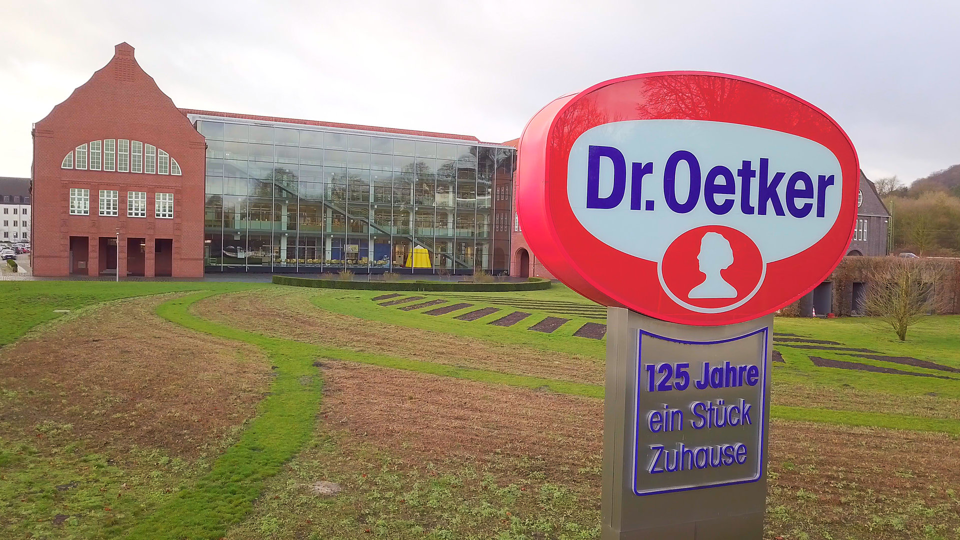 "ZDFzeit: Der große Dr. Oetker-Report - Wie gut sind Pudding, Pizza & Co.?": Konzernzentrale in Bielefeld mit Logo-Schild im Vordergrund.
