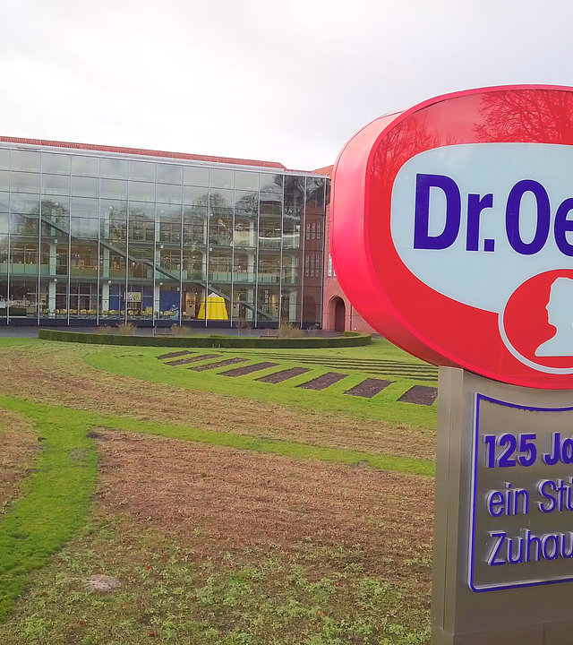 "ZDFzeit: Der große Dr. Oetker-Report - Wie gut sind Pudding, Pizza & Co.?": Konzernzentrale in Bielefeld mit Logo-Schild im Vordergrund.
