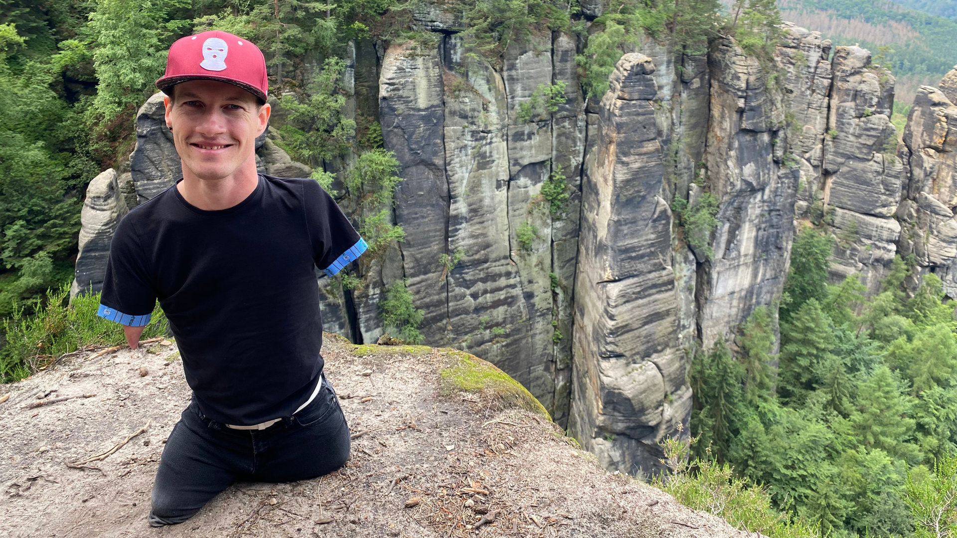 "einfach Mensch: High Hopes - auf zum Gipfel": Janis McDavid befindet sich auf einem Felsen und lacht in die Kamera.