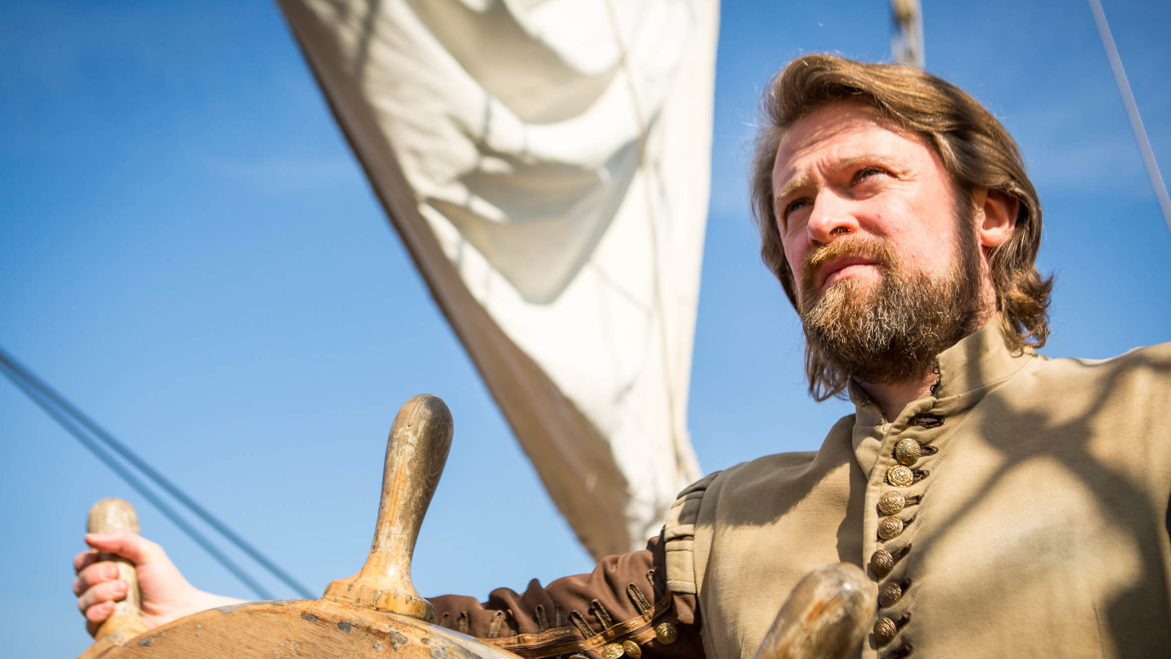 "Terra X: Freibeuter der Meere - Sir Francis Drake" Drake am Steuerrad, unter herrlich blauem Himmel, im Hintergrund weißes Segel.