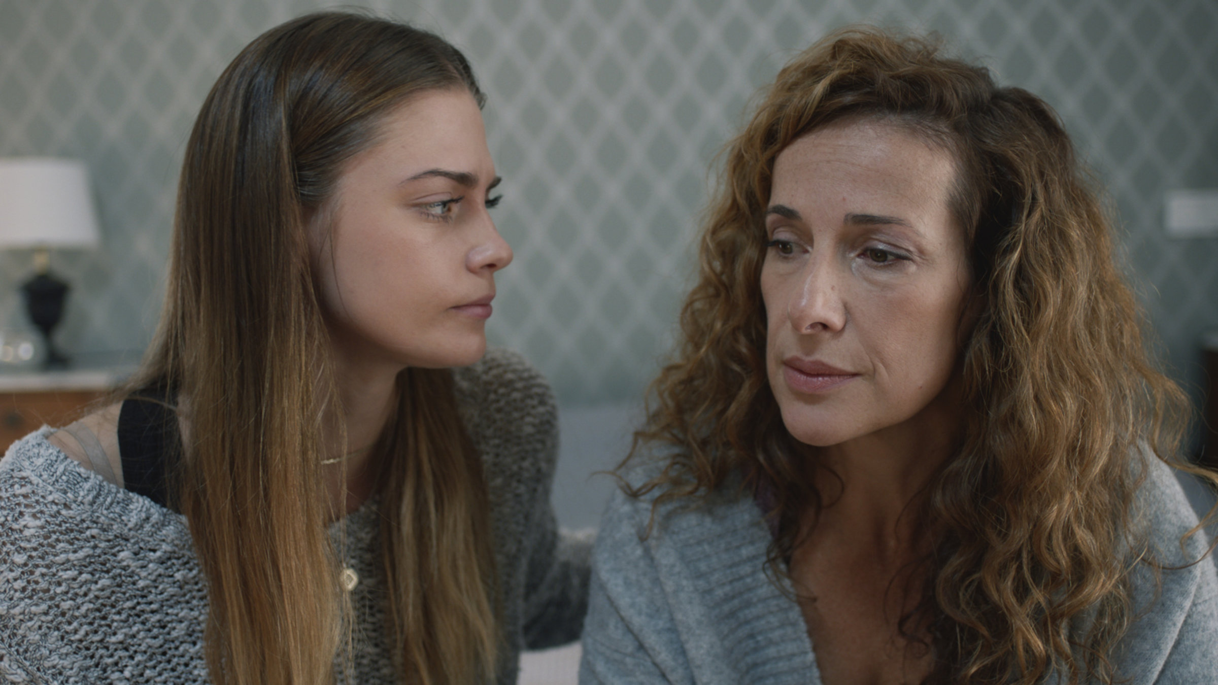 "Professor T. - Das verlorene Kind": Das Au-pair-Mädchen Maren Silke Bäumler (Laura Berlin) sitzt neben Linda Thierse (Clelia Sarto) auf einem Bett und hat ihr die linke Hand tröstend auf die Schulter gelegt. Linda Thierse schaut traurig nach vorne.