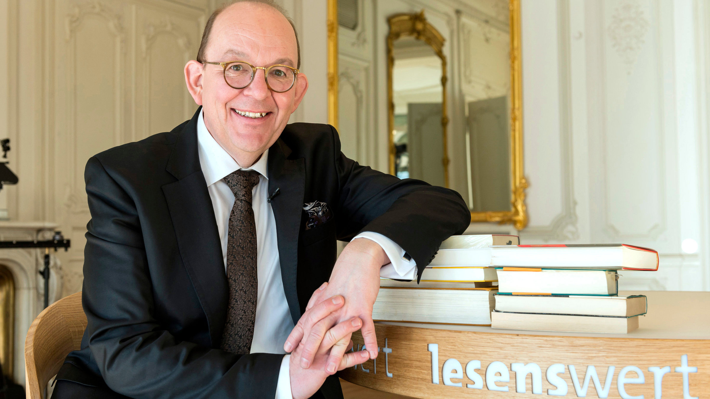 "lesenswert": Denis Scheck sitzt an einem Tisch mit Büchern im Palais Biron, Baden-Baden.