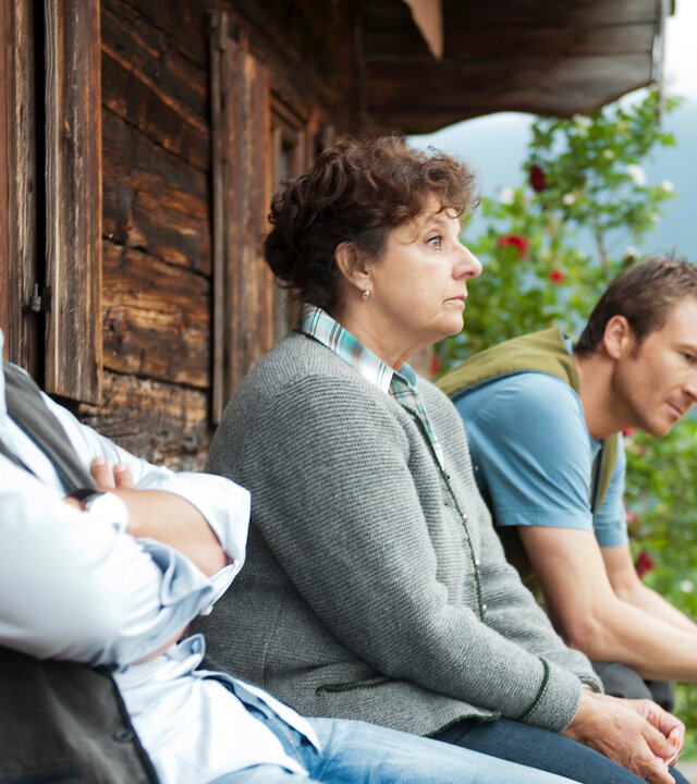 "Der Bergdoktor - Verantwortung": Außenaufnahme - Dr. Martin Gruber (Hans Sigl), Lisbeth Gruber (Monika Baumgartner), Hans Gruber (Heiko Ruprecht) sitzen auf einer Bank an einer Berghütte. Alle drei blicken sehr nachdenklich.