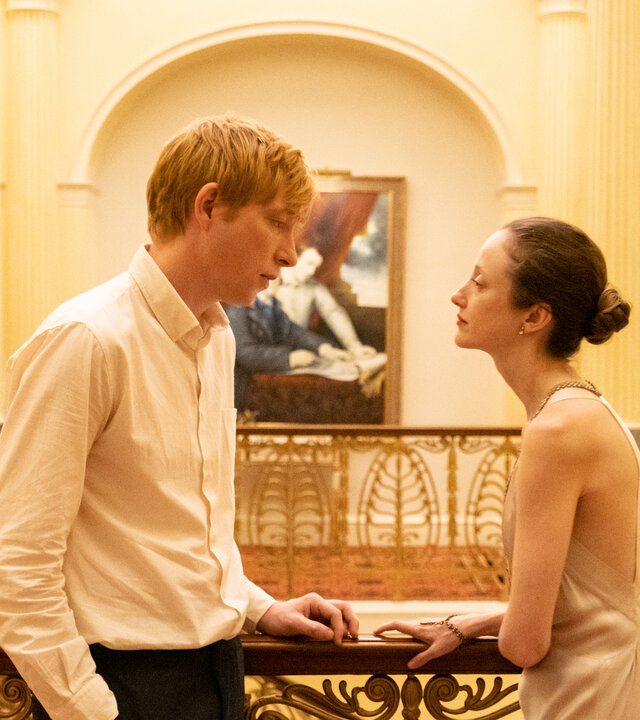 "Alice & Jack - Risiko": Jack (Domhnall Glesson) und Alice (Andrea Riseborouht) stehen sich Innen am Treppengeländer eines wunderschönen Hauses gegenüber. Er steht lässig, mit den Händen in den Taschen da, während sie die Arme schützend verschränkt vor sich hält.