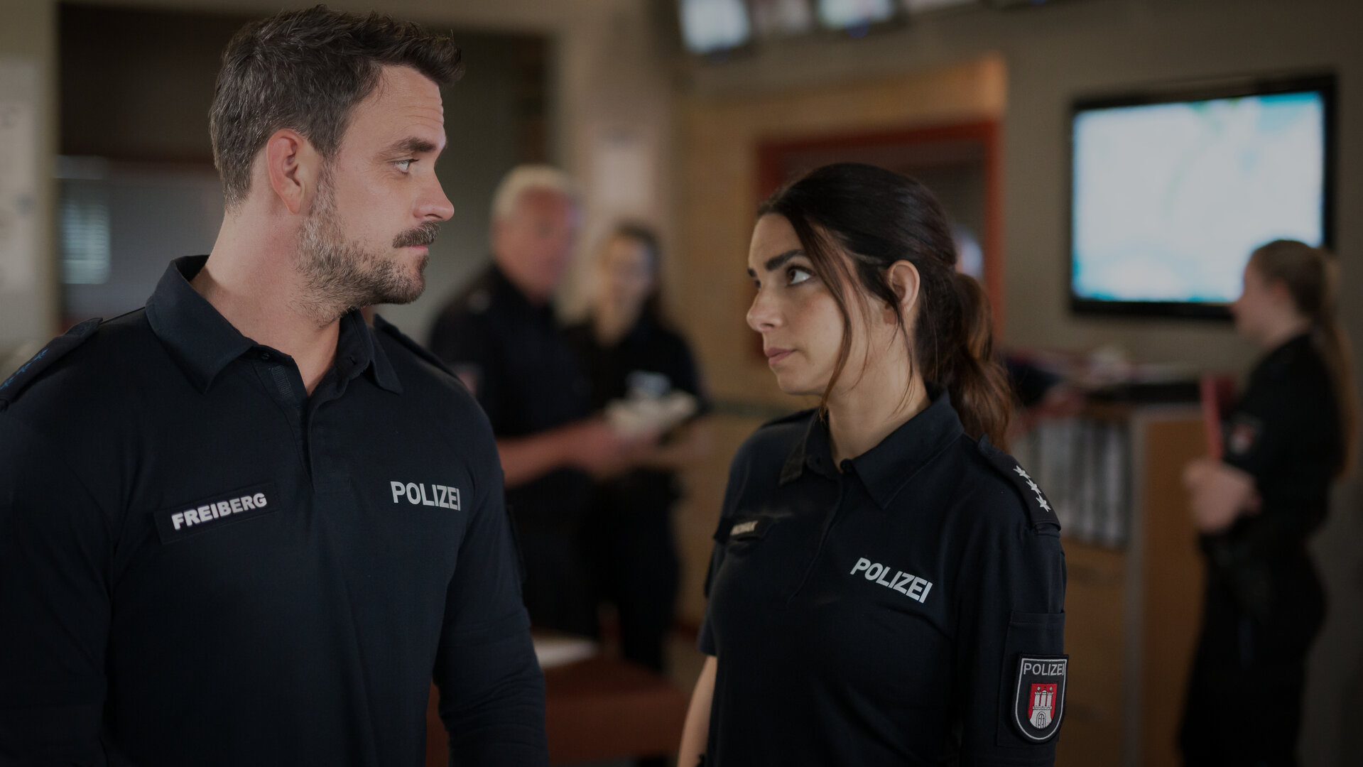 "Notruf Hafenkante - Tage wie dieser": Der Polizist Kris Freiberg (Marc Barthel) und seine Kollegin Isa Nowak (Lilli Hollunder) stehen im Büro des Polizeikommissariats zusammen. Lilli sieht Kris eindringlich an. Er erwidert ihren Blick