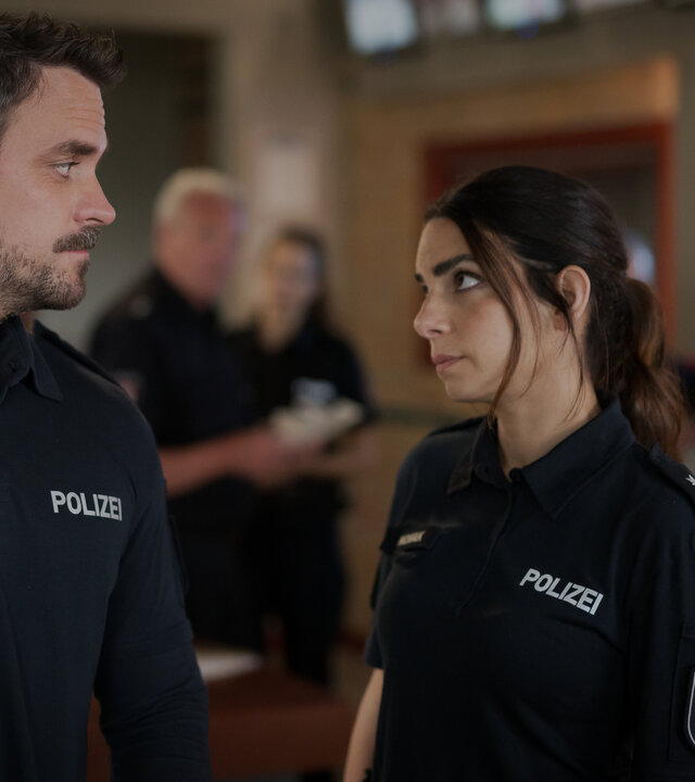 "Notruf Hafenkante - Tage wie dieser": Der Polizist Kris Freiberg (Marc Barthel) und seine Kollegin Isa Nowak (Lilli Hollunder) stehen im Büro des Polizeikommissariats zusammen. Lilli sieht Kris eindringlich an. Er erwidert ihren Blick