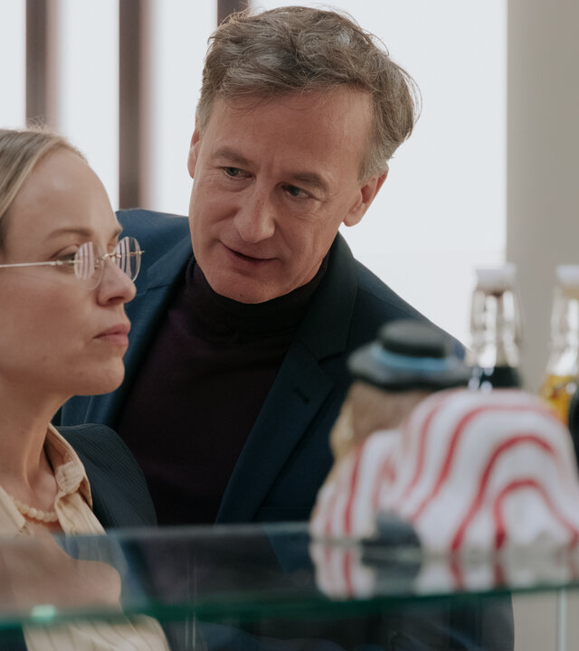 "Nine to Five - Das Amt - Tag 1": Ronja Keller (Friederike Kempter), Amtsleiter Schulenberg (Jan Henrik Stahlberg) und Melissa Seibel (Anna Herrmann) stehen nebeneinander vor der Theke in der Kantine. Georg blickt zu Ronja, Ronja blickt in die Ferne. Melissa beobachtet die beiden.