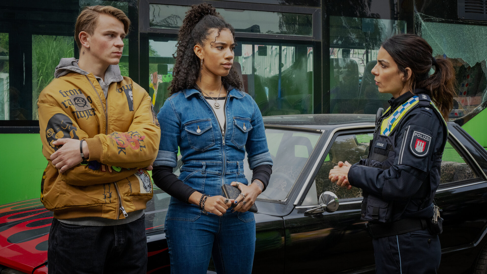 "Notruf Hafenkante - Bruderliebe": Lasse (Dominikus Weileder) und Merle (Joy Ewulu) stehen nebeneinander neben einem Pkw. Sie blicken zu Isa (Lilli Hollunder), die seitlich neben ihnen steht.