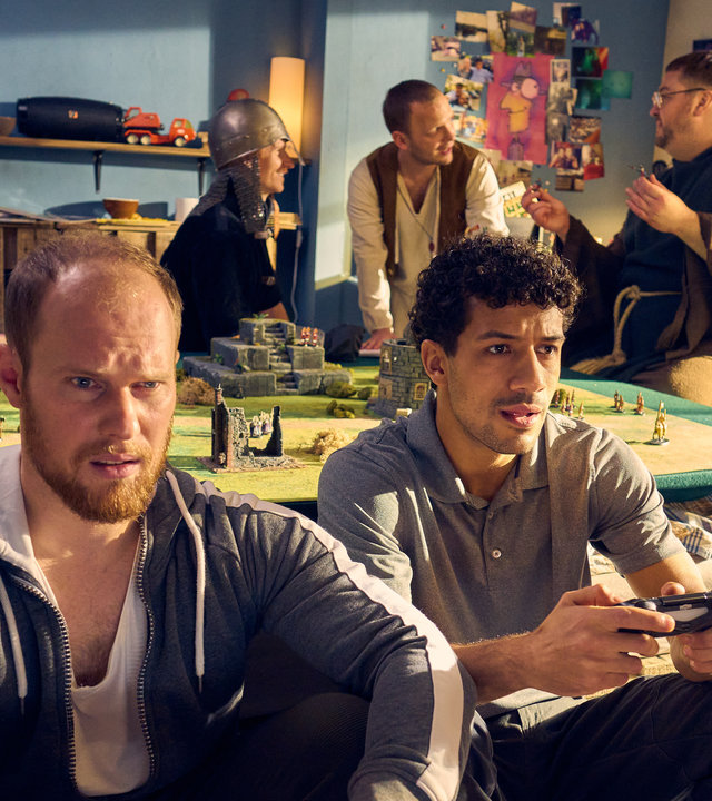 "Ich dich auch! - Der Pömpel": Sven (Sven Daniel Bühler) und Yannik (Rojan Juan Barani) sitzen mit ihren Controllern vor der Spielkonsole. Bennie (Cedric Sprick-Benz), Hauke (Fabian Baecker) und Tüffi (Daniel Zillmann) stehen hinten im Zimmer und unterhalten sich angeregt.