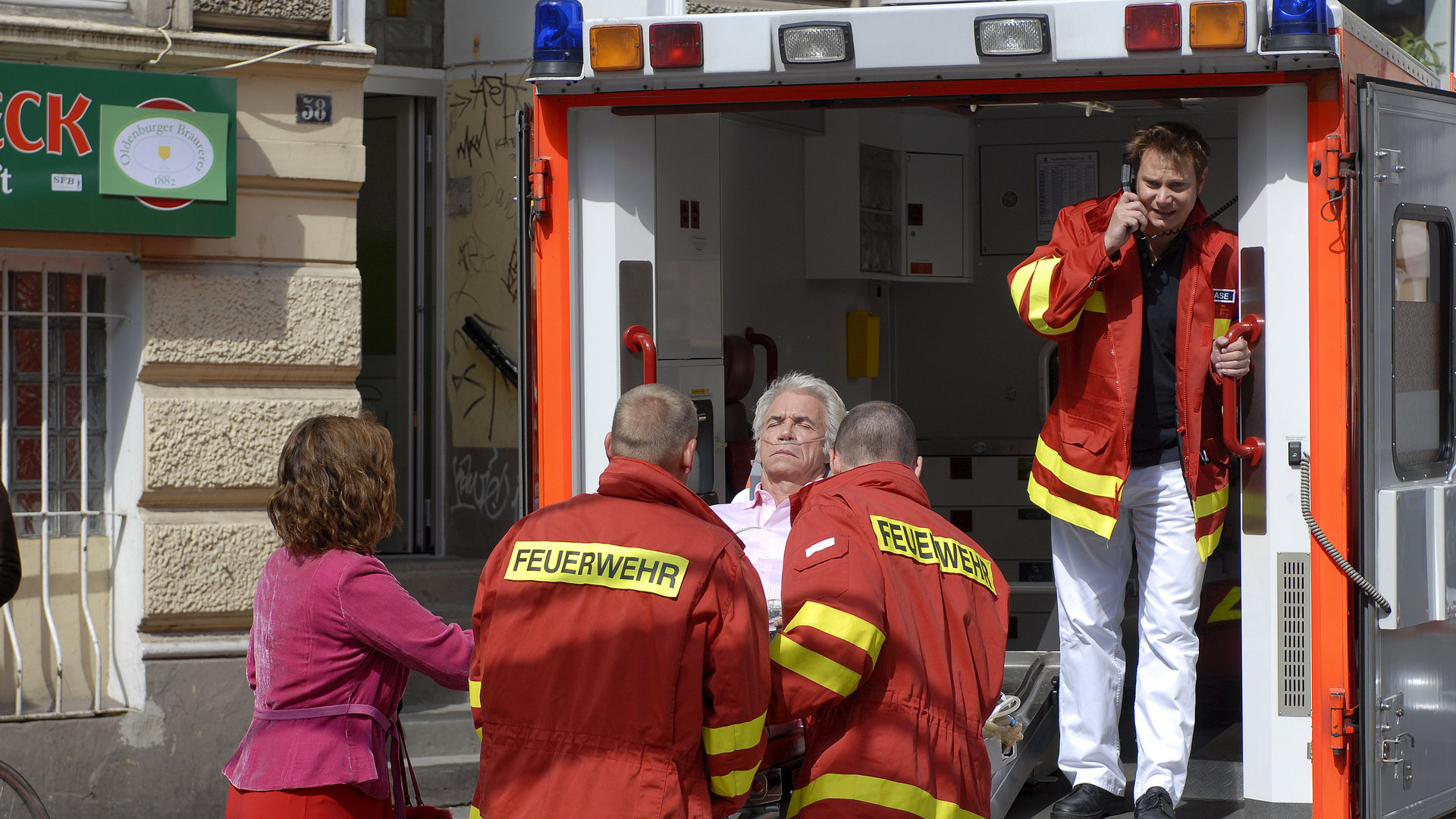 "Notruf Hafenkante - Luckys letzter Coup": Lucky (Wolf Roth) wird in den Krankenwagen verladen. Neben ihm steht seine Frau Manuela (Edda Leesch). Notarzt Dr. Haase (Fabian Harloff) steht im Krankenwagen und telefoniert.