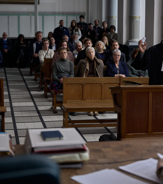 "Elixir – The Pain Killers - Deals": Hamza Toumi (Walid Benmbarek) steht in einem voll besetzten Gerichtssaal hinter dem Anwaltspult und gestikuliert. Im Vordergrund ist die Richterin von hinten im Anschnitt zu sehen.