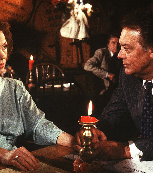 "Die Schwarzwaldklinik - Alles Theater": Christa (Gaby Dohm) und ihr Mann Prof. Brinkmann (Klausjürgen Wussow) sitzen im Restaurant am Tisch und unterhalten sich.