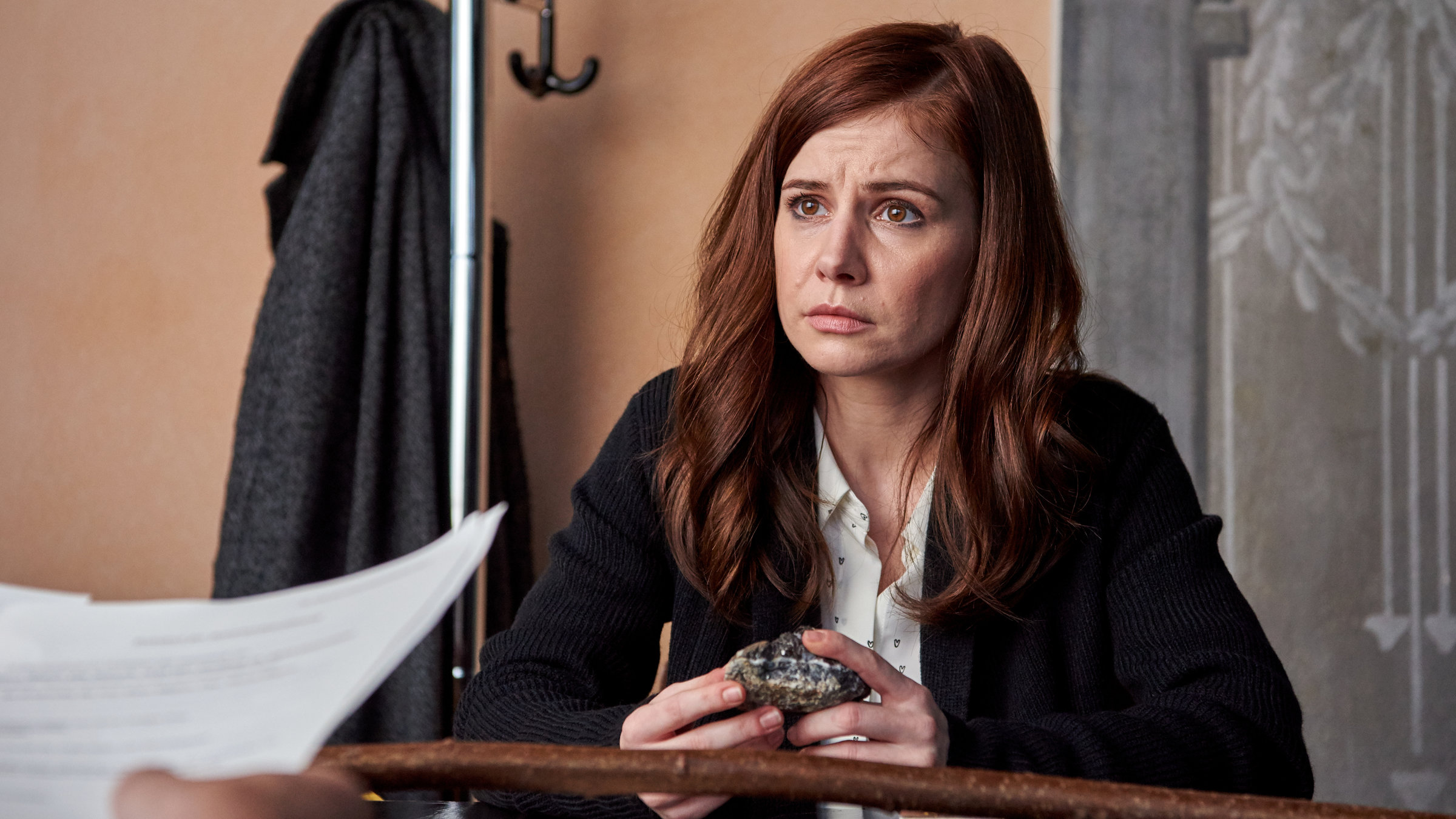 "Schattengrund - Ein Harz-Thriller": Nicola Wagner (Josefine Preuß) sitzt beim Notar am Schreibtisch. In der Hand hält sie einen Stein, ihr Blick ist nach vorne gerichtet.