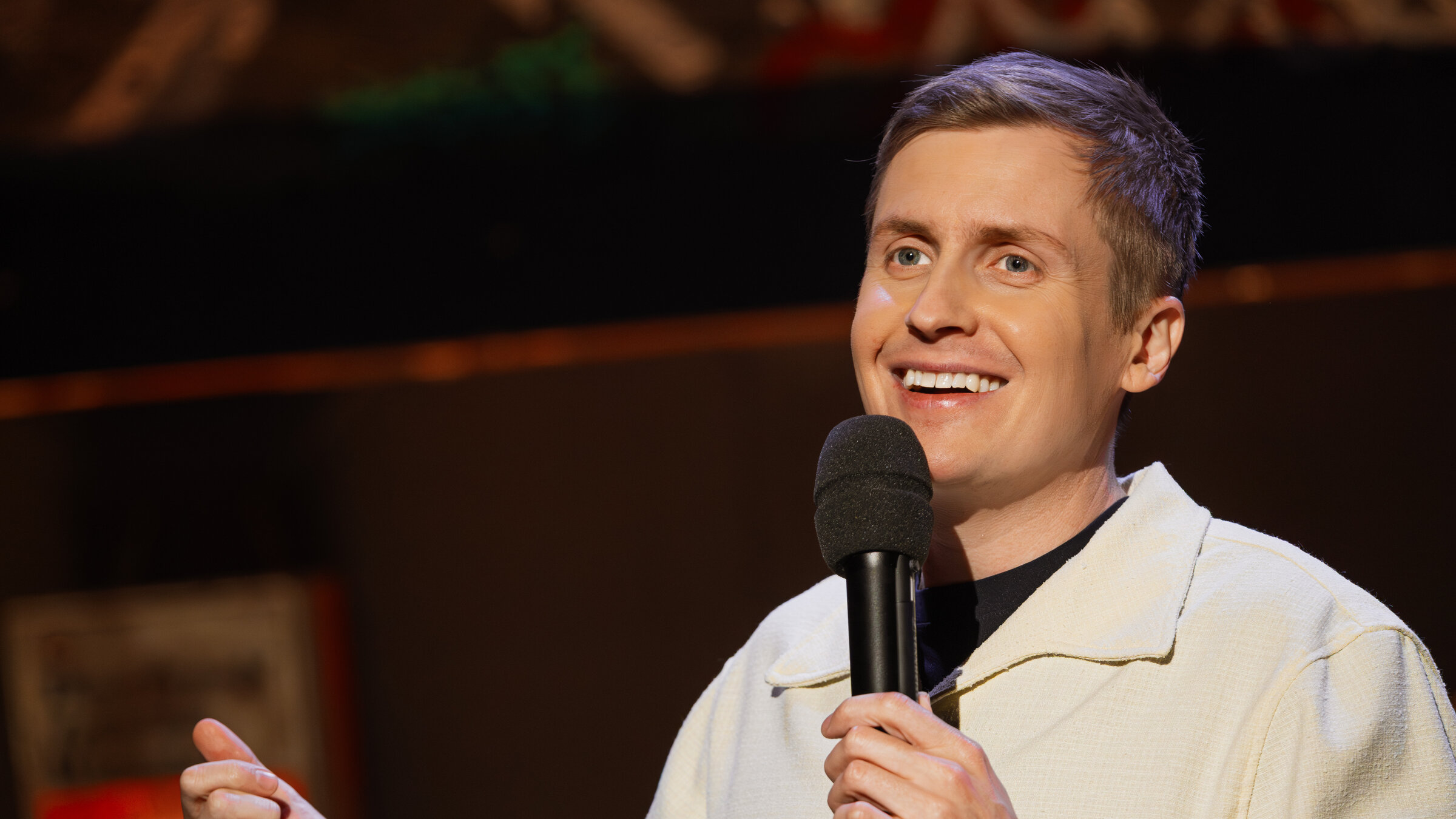 "Till Reiners` Happy Hour": Der Stand-Up-Comedian Till Reiners steht mit einem Mikrofon in der Hand auf der Bühne und spricht zum Publikum.