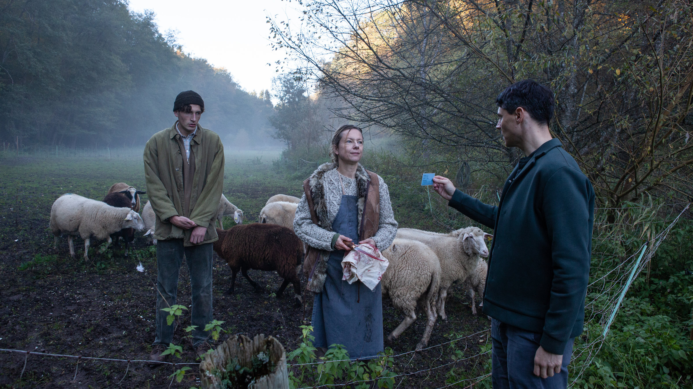 “SOKO Stuttgart – Geisterjagd“: Rico Sander (Benjamin Strecker) steht seitlich vor einem Weidezaun aus Draht und zeigt seinen Dienstausweis. Ihm gegenüber – hinter dem Zaun – steht die Schäferin Franziska Oberlehner (Susanne Hoss). Sie hält ein weißes Tuch und ein Messer in der Hand. Auf beidem sieht man Blutspuren. Schräg hinter ihr steht ihr Sohn, Hanno Oberlehner (Levin Liam). Er zupft sich unruhig am Jackenärmel und hat einen abwesenden Gesichtsausdruck. Direkt hinter ihnen tummeln sich weiße und braune Schafe. Im Hintergrund liegt eine nebelverhangene Wiese, eingerahmt von Büschen und Bäumen.