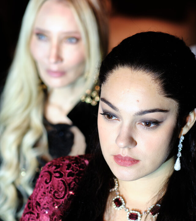 "Take the Money and Run - One Dream": Ruja Ignatova (Nilam Farooq) steht in einem glitzernden Kleid und auffälligem Schmuck im Vordergrund, ihr Blick ist konzentriert nach vorne gerichtet. Hinter ihr stehen Elva Gunnarsdottir (Tina Balthazar) und Jonas Kurth (László Branko Breiding).