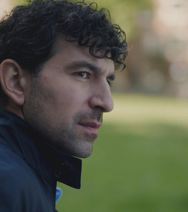 "Blind Sherlock - Miese Ratte": Yaqub (Sinan Eroglu) steht im Grünen und blickt zur Seite. Er macht einen skeptischen Eindruck.