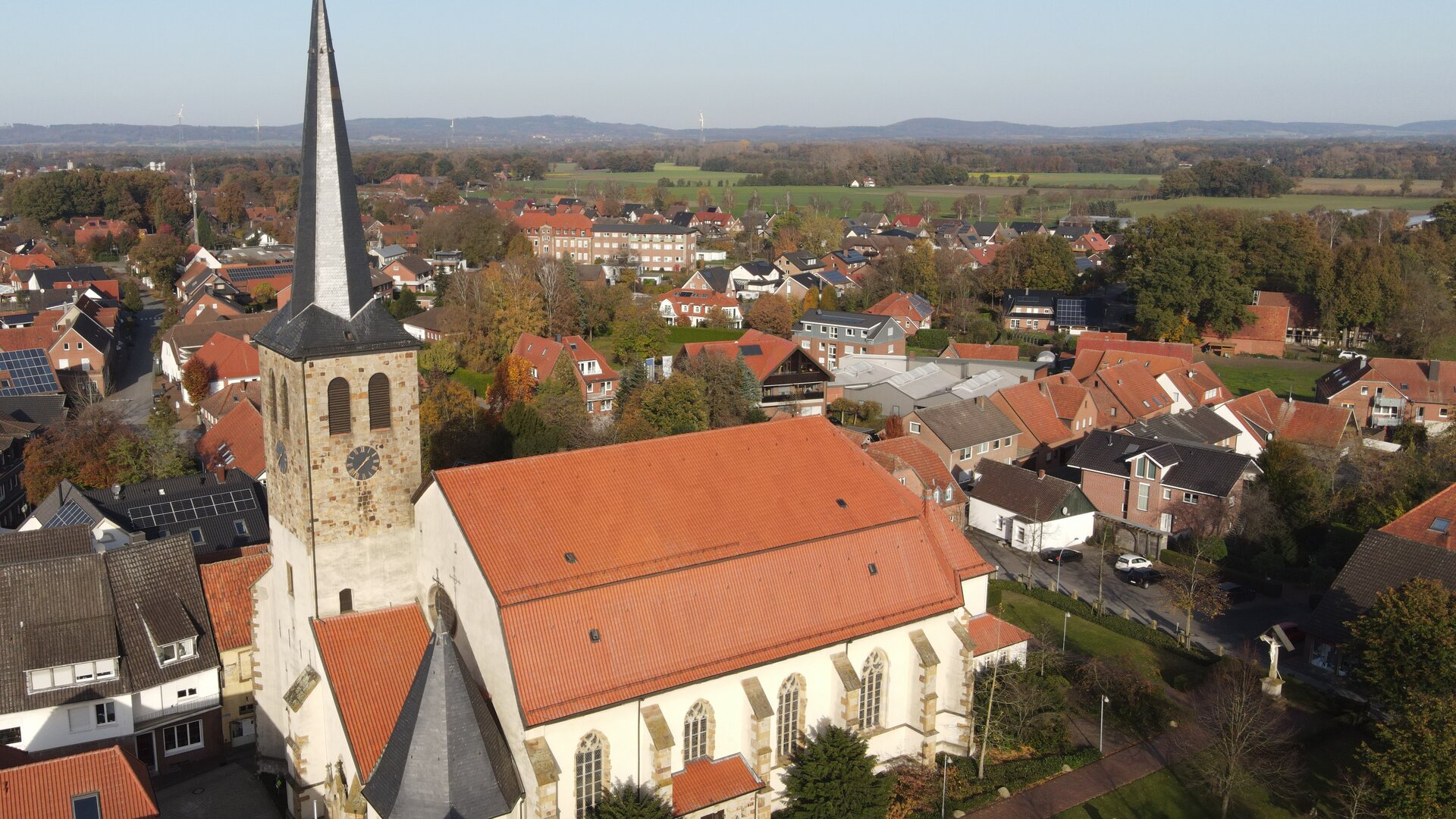 "Katholischer Gottesdienst - Ich freue mich auf dich!": Luftaufnahme der Pfarrkirche St. Johannis in Glandorf mit umliegenden Häusern