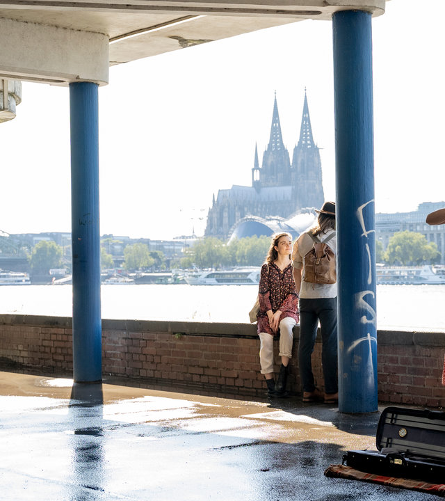 "SOKO Köln - Eingeschüchtert": In einem Parkhaus am Rhein, mit Blick auf den Kölner Dom, spielt Pola Huth (Alissa Jung) Geige. Rechts von ihr, mit den Händen in den Hosentaschen, steht Hauptkommissar Matti Wagner (Pierre Besson).