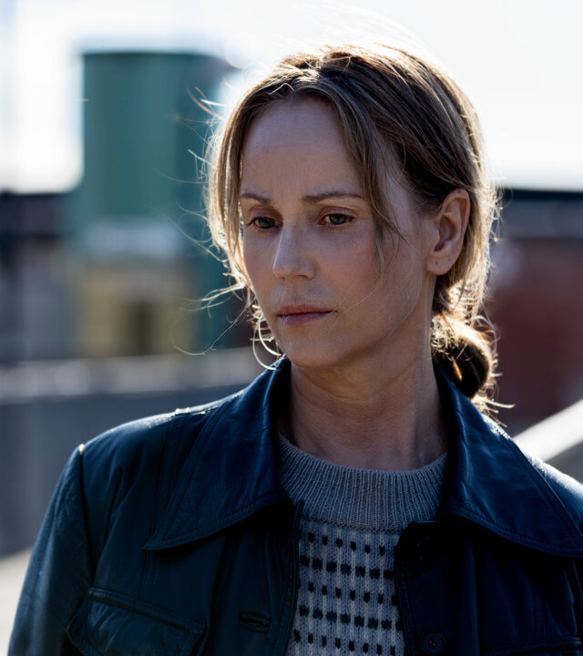 "Iris - Die Wahrheit – Verbockt": Iris (Sofia Helin) steht draußen vor mehreren Gebäuden und einer Fußgängerbrücke. Sie wirkt nachdenklich.