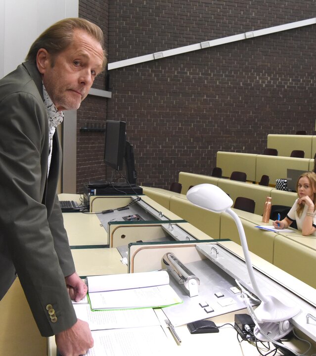 "SOKO Wien - Was wäre, wenn...?": Spurensicherer Franz Wohlfahrt (Helmut Bohatsch) steht an einem Pult im Hörsaal. Vor ihm sitzen Studenten (Komparsen), die sich Notizen machen.