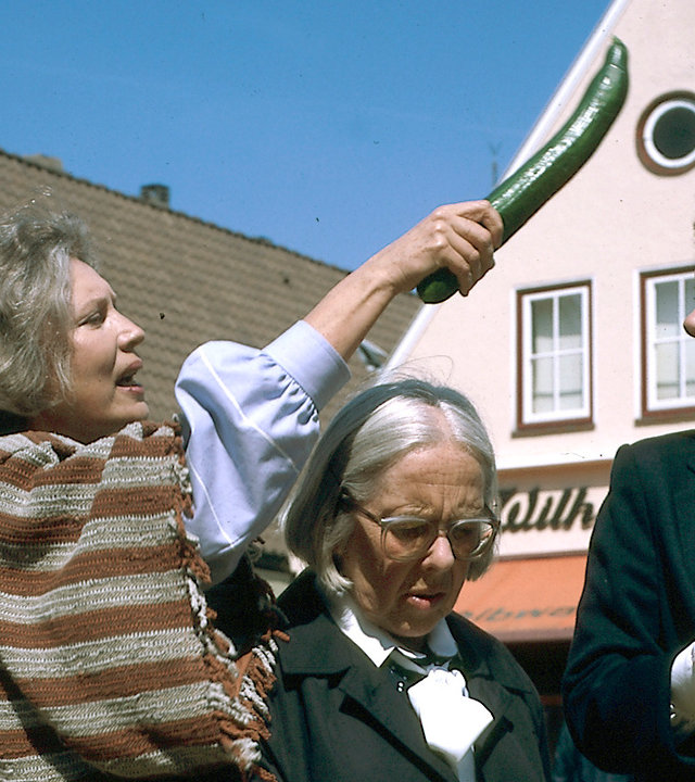 "Der Landarzt - Die Liebe, die Liebe": Olga Mattiesen (Antje Weisgerber) schlägt mitten auf einem Marktplatz Thea (Evelyn Hamann) mit einer Gurke auf den Kopf. Zwischen ihnen steht die irritierte Berta (Gerda Gmelin).