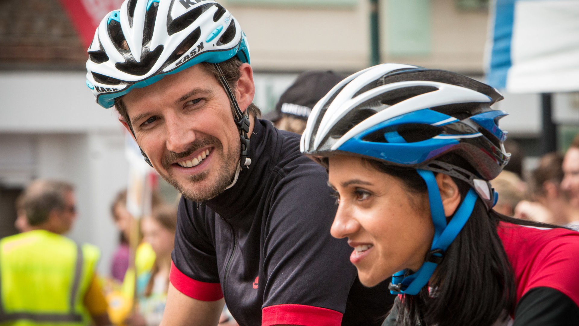 "Inspector Barnaby - Der Tod radelt mit": DS Charlie Nelson (Gwilym Lee) lächelt Dr. Kam Karimore (Manjinder Virk) zu. Beide warten, mit Helm und Trikot auf den Startschuss beim Radrennen.