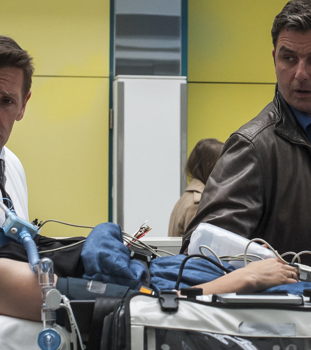 "Der Bergdoktor - Ein kaltes Herz (1)": Im Krankenhaus liegt Luisa Fischer (Friederike Linke) auf einer Liege. Neben ihr stehen Dr. Alexander Kahnweiler (Mark Keller) und Martin Gruber (Hans Sigl), die sie beide besorgt anschauen.