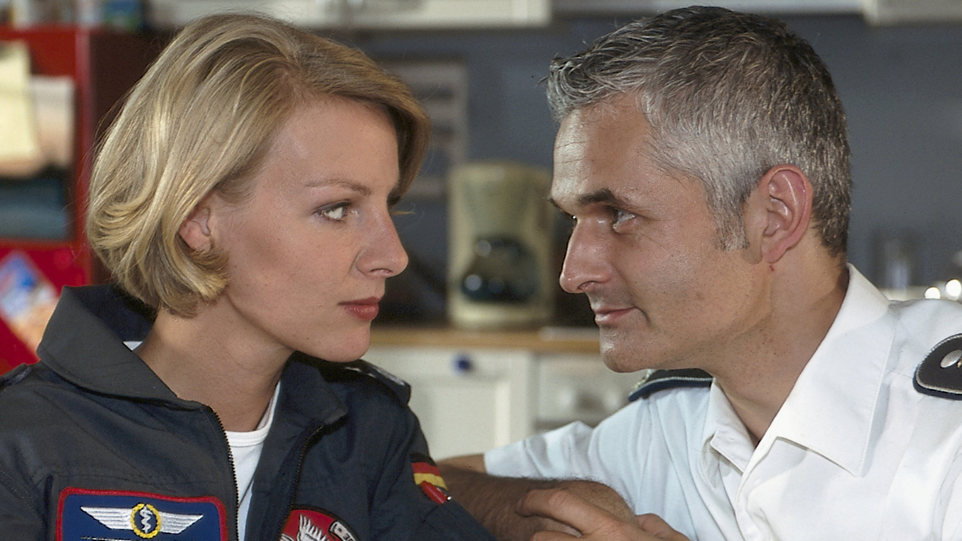 "Die Rettungsflieger - In der Falle": Dr. Rieckhoff (Norbert Ghafouri) und Dr. Petersen (Marlene Marlow) sitzen nebeneinander und schauen sich in die Augen.