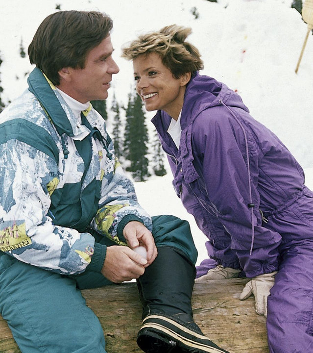 "Zwei Münchner in Hamburg - Zum Heiraten gehören zwei": Julia (Ushi Glas) und Ralf (Elmar Wepper) sitzen lächelnd auf einem Baumstamm in einer verschneiten Landschaft. Beide tragen Ski-Kleidung.