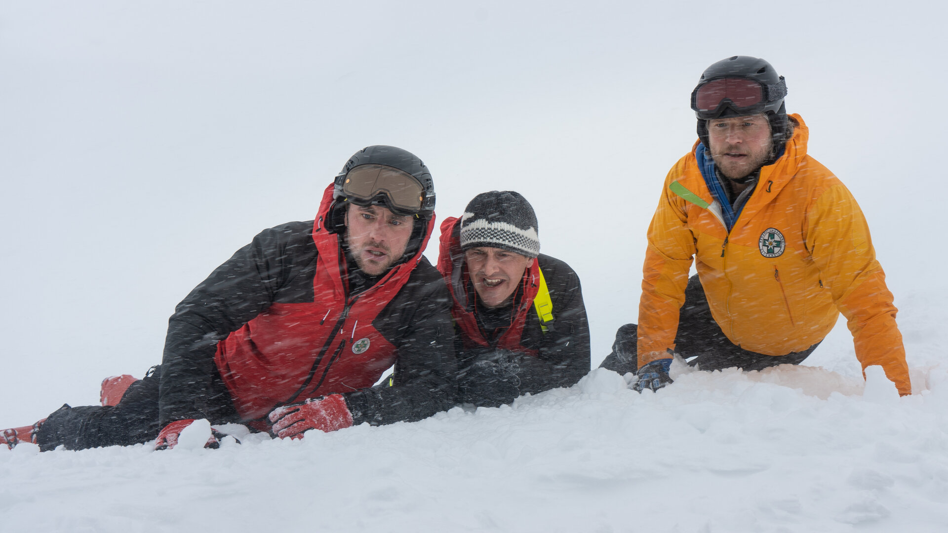 "Die Bergretter: Eiskalte Wahrheit": Simon (Ferdinand Seebacher), Rudi (Michael Pascher) und Markus (Sebastian Ströbel) liegen in voller Montur im Schnee, ihre Blicke sind bestürzt. Es schneit.