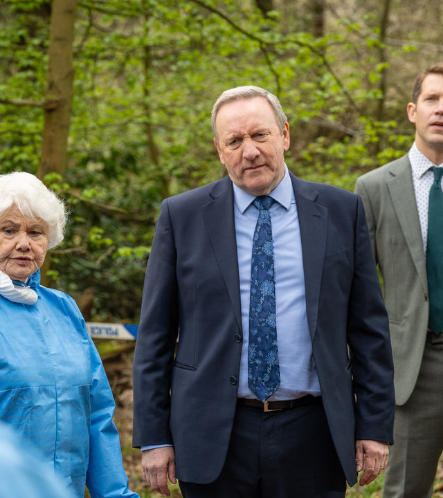 "Inspector Barnaby - Das Buch Bertram": Fleur Perkins (Annette Badland), Detective Chief Inspector John Barnaby (Neil Dudgeon und Detective Constable Jamie Winter (Nick Hendrix) stehen nebeneinander im Wald. Hinter ihnen ist ein Absperrband der Polizei gespannt.