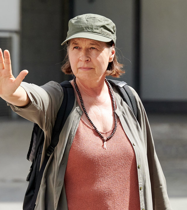 "Aufgestaut - Margot": Margot steht auf der Straße und streckt ihre rechte Hand entschlossen nach vorne.