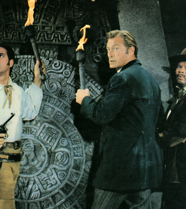 "Die Pyramide des Sonnengottes": Dr. Karl Sternau (Lex Barker), Graf Alfonso (Gérard Barray) und André Hasenpfeffer (Ralf Wolter) haben Fackeln in den Händen und schauen sich um. Sie stehen vor einem riesigen steinernen Inka-Ornament.