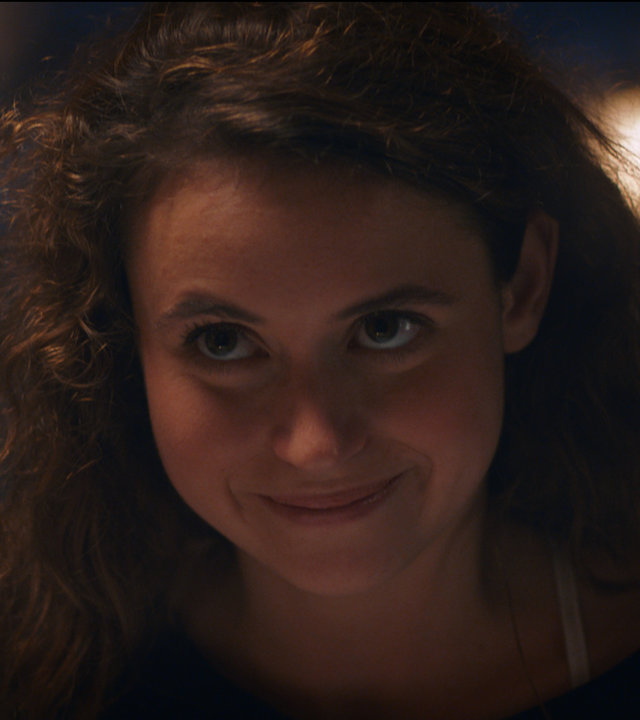 "Sense of Tumour - Agapornis": Hanne (Marthe Schneider) sitzt am Tisch in einem schicken Restaurant und schaut amüsiert drein.