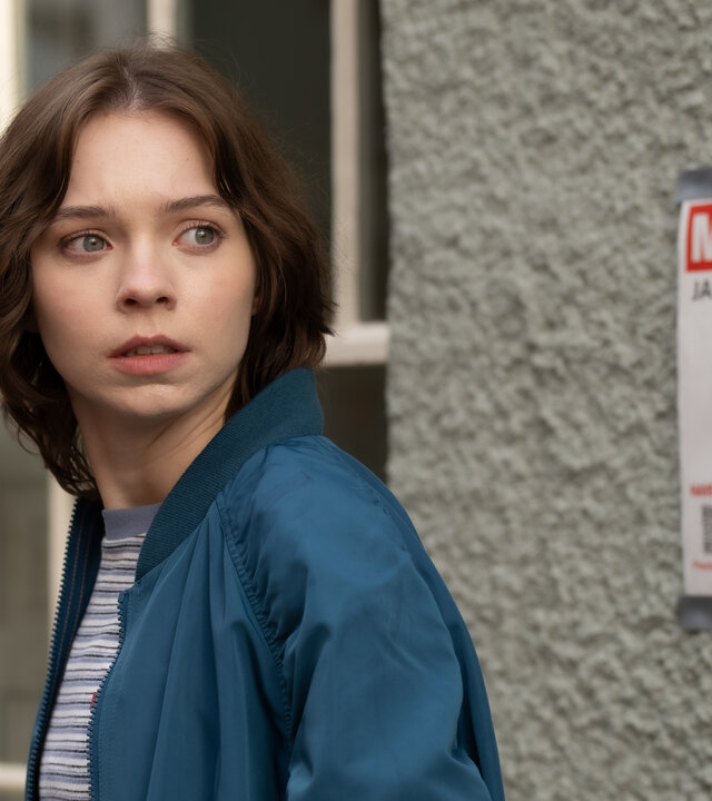 "A Good Girl’s Guide to Murder – Das Verschwinden von Jamie Reynolds": Pip Fitz-Amobi (Emma Myers) steht in einer Gasse neben einem "Missing"-Poster von Jamie Reynolds. Sie schaut angespannt zur Seite.