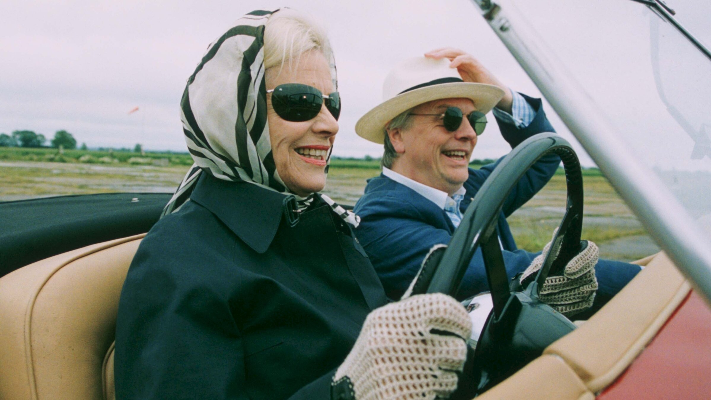 "Inspector Barnaby - Der Tod und die Lady": Isobel Hewitt (Honor Blackman) und Quentin Roka (Philip Franks) fahren lachend in einem offenem Auto durch die Felder.